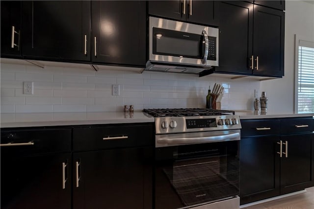 kitchen featuring decorative backsplash, stainless steel appliances, light countertops, and dark cabinets