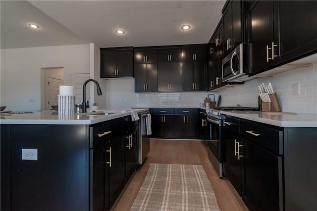 kitchen with a sink, dark cabinetry, stainless steel appliances, light wood-style floors, and light countertops