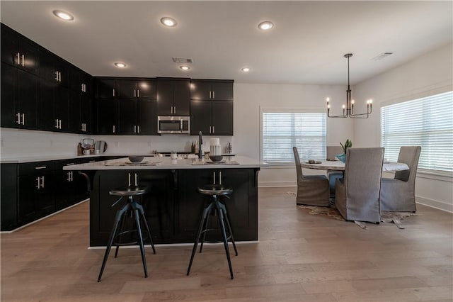 kitchen with stainless steel microwave, a kitchen bar, light wood-style floors, and dark cabinets