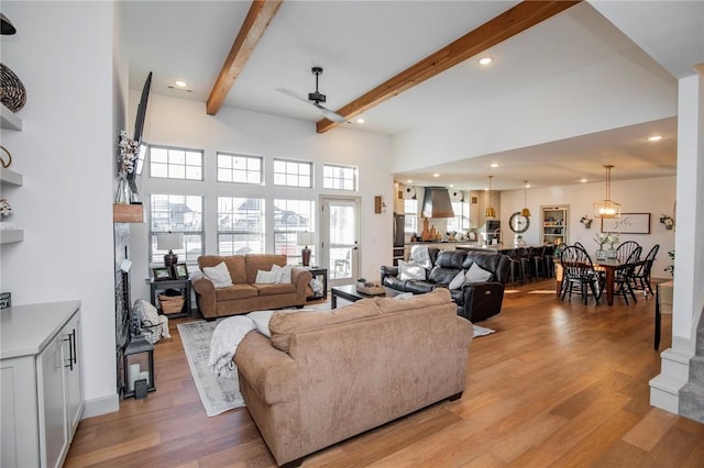 living room featuring beamed ceiling, ceiling fan, a high ceiling, and light wood-type flooring