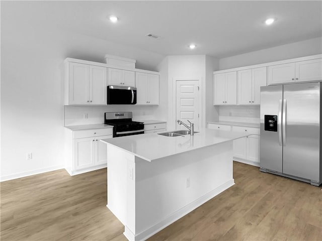 kitchen with sink, a kitchen island with sink, stainless steel appliances, white cabinets, and light wood-type flooring