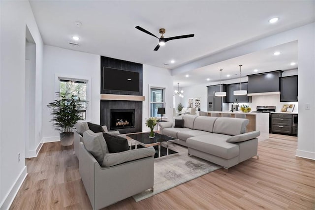 living room with a large fireplace, sink, ceiling fan, and light hardwood / wood-style flooring