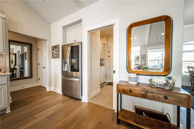 interior space featuring stainless steel fridge, hardwood / wood-style floors, white cabinets, stainless steel fridge with ice dispenser, and vaulted ceiling