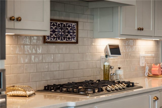 kitchen featuring light stone counters, white cabinets, decorative backsplash, and stainless steel gas stovetop