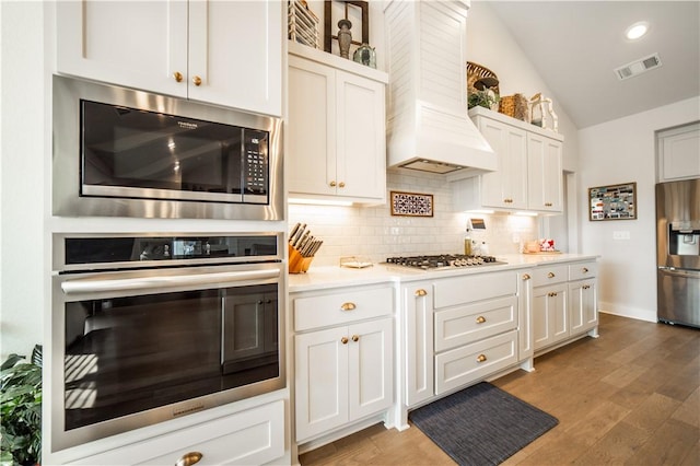 kitchen with premium range hood, lofted ceiling, appliances with stainless steel finishes, dark hardwood / wood-style flooring, and white cabinets