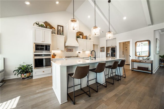 kitchen with white cabinetry, decorative light fixtures, stainless steel appliances, and a large island with sink