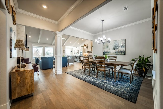 dining area featuring crown molding, wood-type flooring, vaulted ceiling, a chandelier, and ornate columns