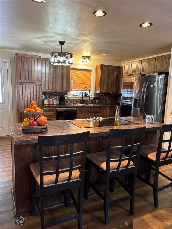 kitchen with sink, dark wood-type flooring, appliances with stainless steel finishes, a kitchen breakfast bar, and a kitchen island