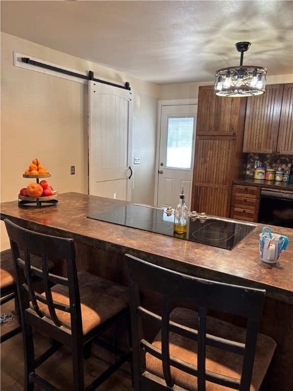 interior space with tasteful backsplash, a breakfast bar area, dark hardwood / wood-style flooring, black appliances, and a barn door