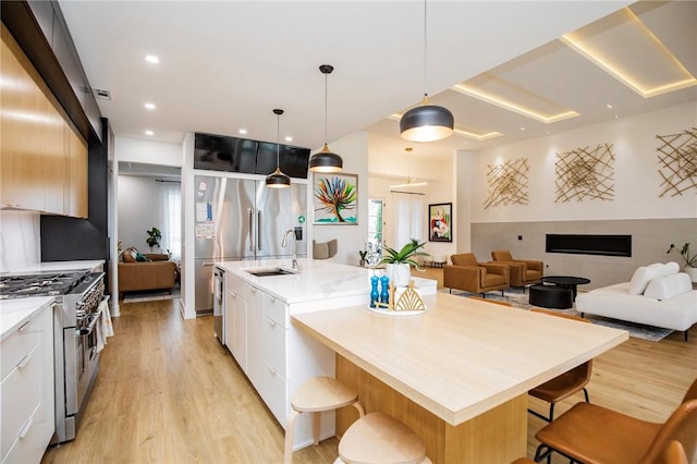 kitchen with range with two ovens, an island with sink, pendant lighting, and white cabinets