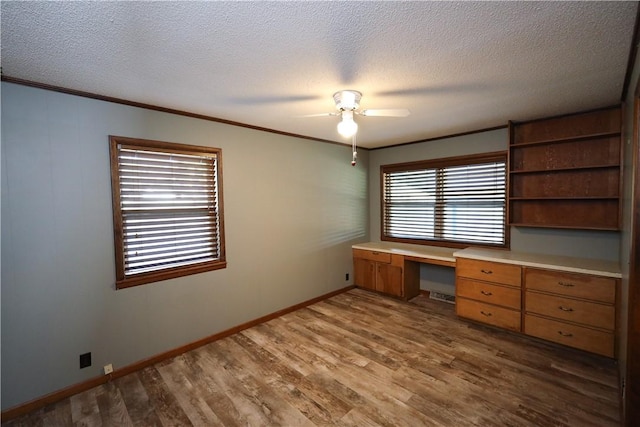 unfurnished office featuring hardwood / wood-style floors, built in desk, ornamental molding, and ceiling fan