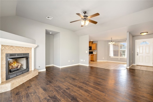 unfurnished living room with ceiling fan with notable chandelier, lofted ceiling, a tiled fireplace, and hardwood / wood-style floors