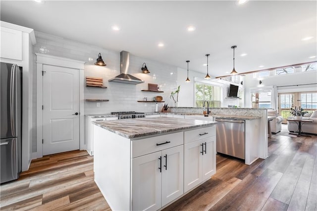 kitchen featuring white cabinets, a center island, wall chimney exhaust hood, and appliances with stainless steel finishes