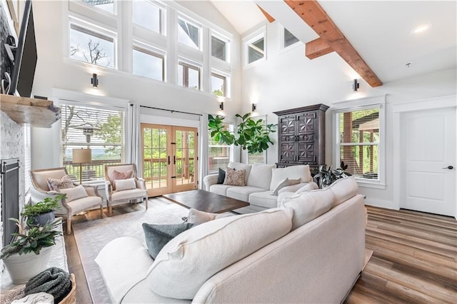 living room featuring a towering ceiling, a fireplace, hardwood / wood-style flooring, beam ceiling, and french doors