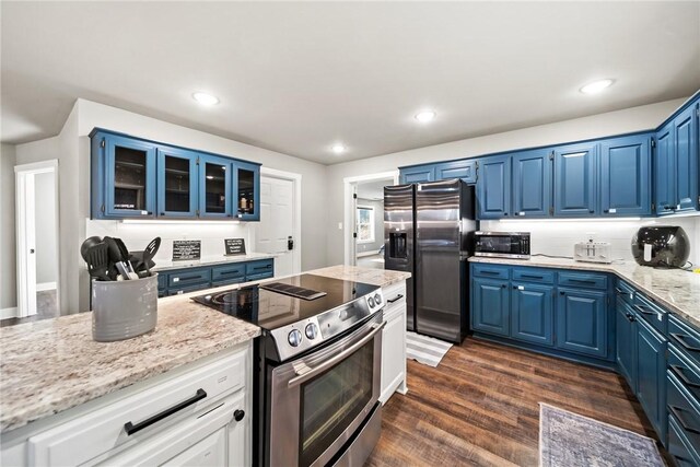 kitchen with appliances with stainless steel finishes, dark hardwood / wood-style flooring, blue cabinets, and light stone countertops