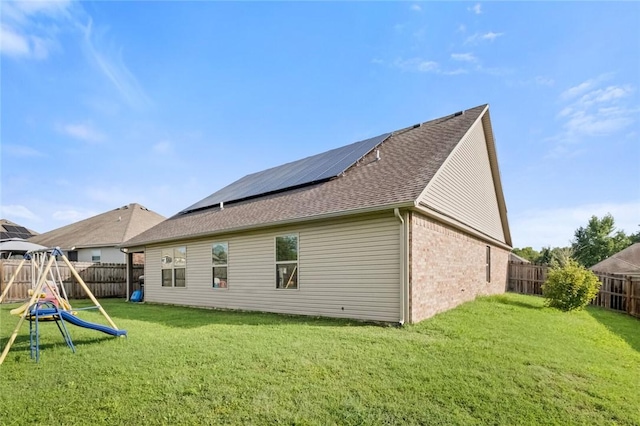 back of property with a playground, a lawn, and solar panels