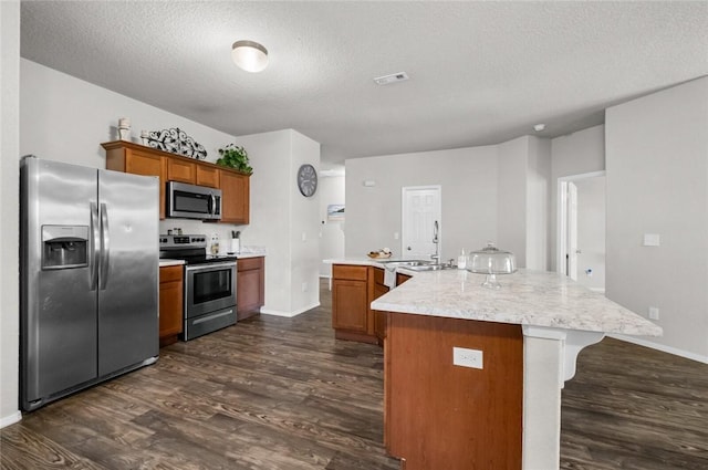 kitchen featuring dark hardwood / wood-style floors, an island with sink, a textured ceiling, and appliances with stainless steel finishes