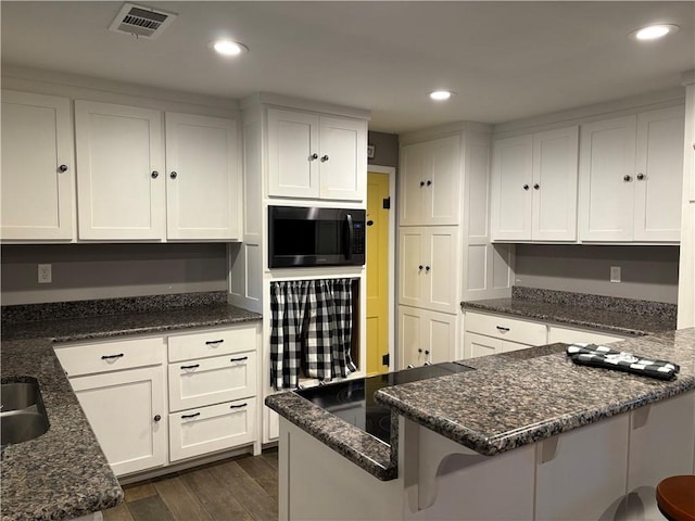 kitchen with a peninsula, white cabinets, dark wood-type flooring, built in microwave, and visible vents