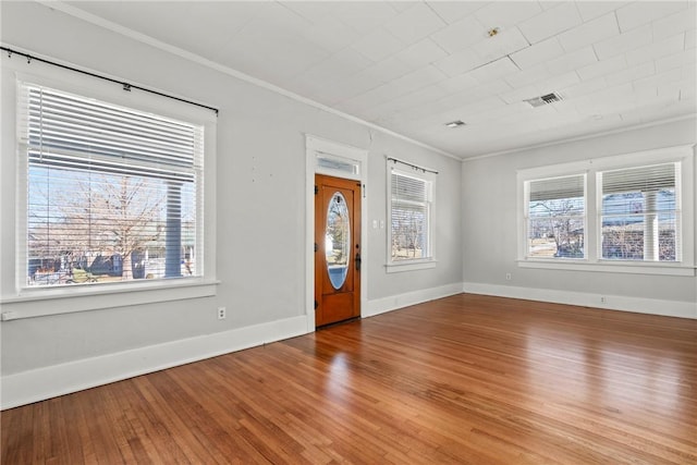 empty room featuring wood-type flooring, a wealth of natural light, and crown molding