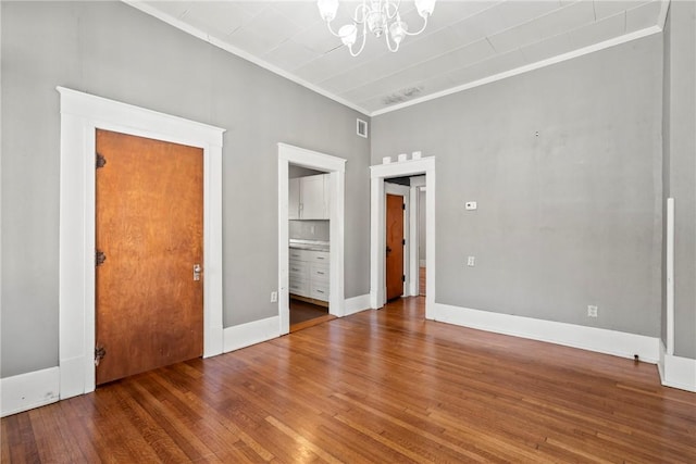 unfurnished bedroom featuring wood-type flooring, ornamental molding, a chandelier, and ensuite bathroom