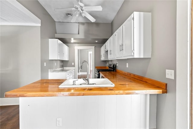 kitchen featuring butcher block counters, sink, stainless steel range with gas cooktop, kitchen peninsula, and white cabinets