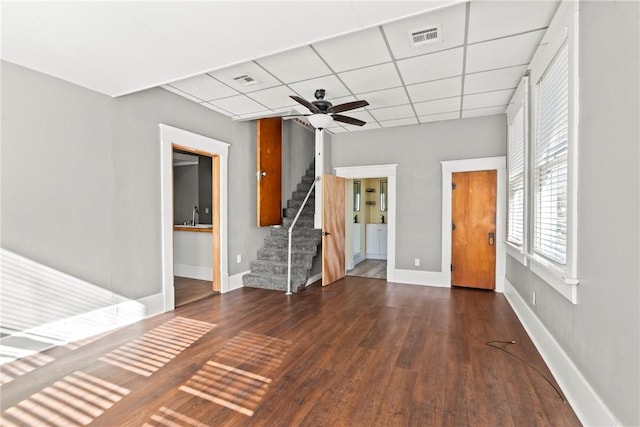 unfurnished living room with a drop ceiling, sink, dark hardwood / wood-style floors, and ceiling fan