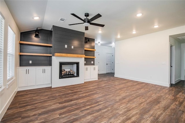 unfurnished living room with dark wood-type flooring, ceiling fan, built in shelves, and vaulted ceiling