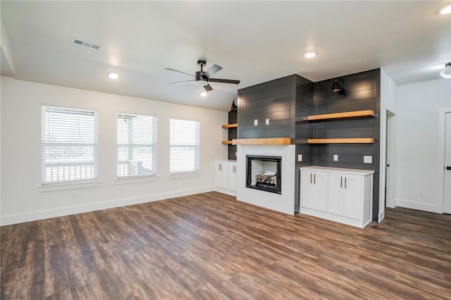 unfurnished living room with dark wood-type flooring, a large fireplace, and ceiling fan