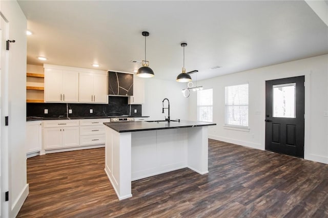 kitchen featuring a kitchen island with sink, sink, white cabinets, and decorative light fixtures