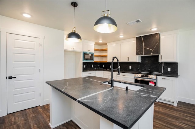 kitchen with built in microwave, hanging light fixtures, an island with sink, oven, and white cabinets