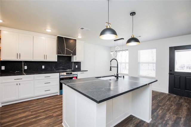 kitchen with decorative light fixtures, sink, white cabinets, a kitchen island with sink, and wall chimney exhaust hood