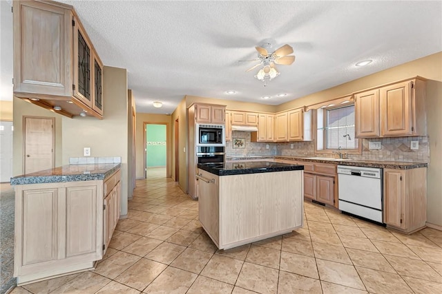 kitchen with light brown cabinetry, stainless steel oven, black microwave, white dishwasher, and a kitchen island