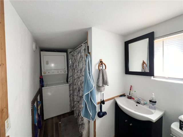 bathroom featuring vanity, stacked washer and clothes dryer, hardwood / wood-style floors, and toilet