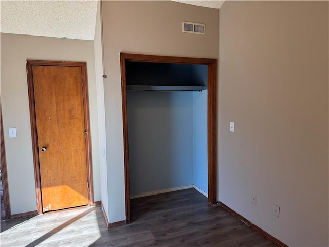 unfurnished bedroom featuring dark hardwood / wood-style floors, vaulted ceiling, a closet, and a textured ceiling