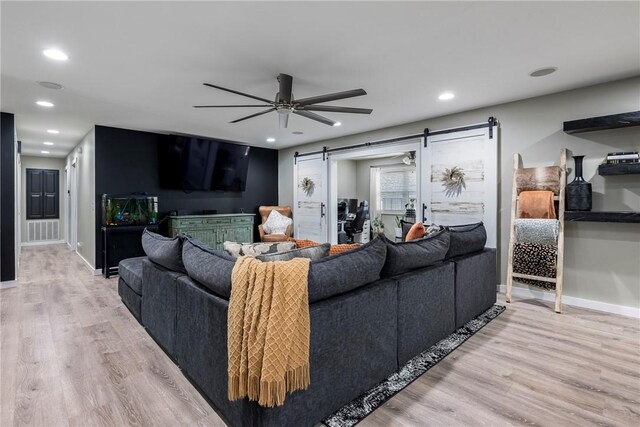 living room with ceiling fan, a barn door, and light hardwood / wood-style floors