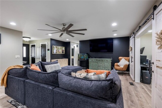 living room with ceiling fan, a barn door, and light wood-type flooring