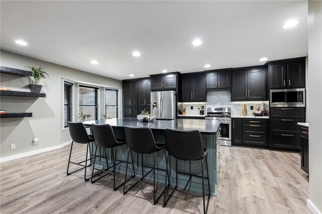 kitchen with appliances with stainless steel finishes, a breakfast bar, an island with sink, backsplash, and light hardwood / wood-style floors