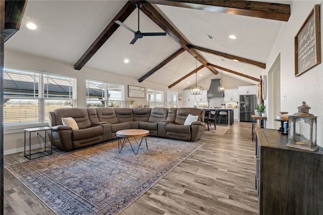 living room with plenty of natural light, ceiling fan with notable chandelier, light hardwood / wood-style flooring, and vaulted ceiling with beams