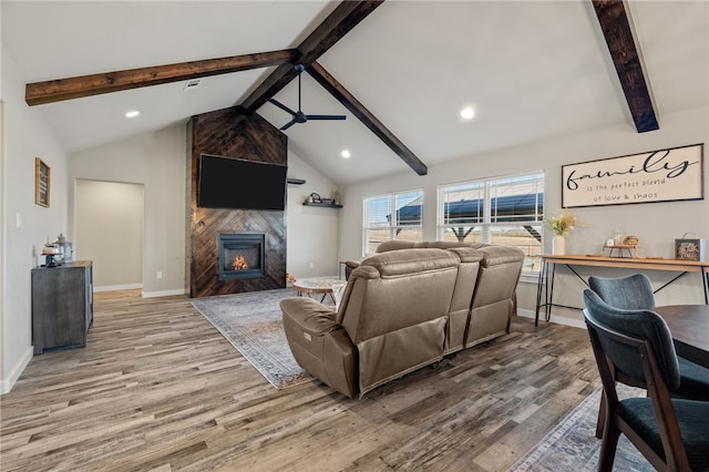 living room featuring a tiled fireplace, hardwood / wood-style flooring, ceiling fan, and lofted ceiling with beams