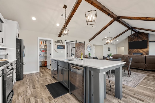 kitchen featuring pendant lighting, stainless steel appliances, lofted ceiling with beams, a center island with sink, and a barn door