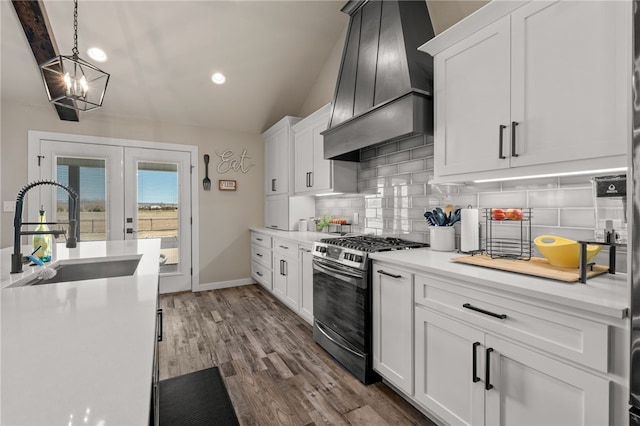 kitchen with premium range hood, stainless steel gas range, sink, white cabinetry, and hanging light fixtures