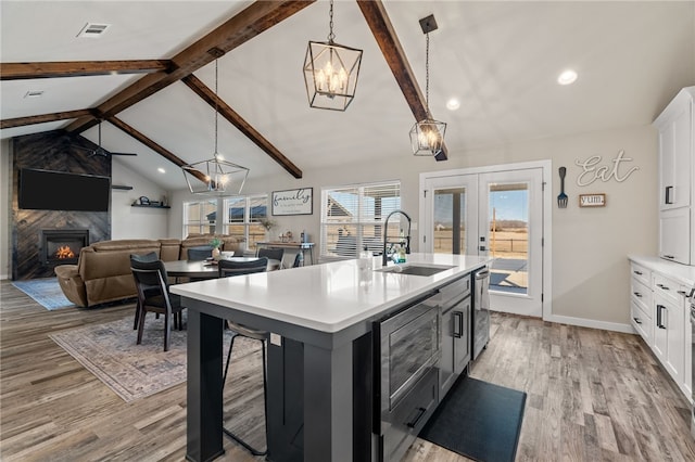 kitchen featuring pendant lighting, vaulted ceiling with beams, an island with sink, and white cabinets