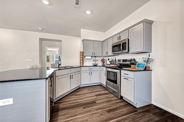 kitchen with gray cabinets, sink, dark hardwood / wood-style flooring, kitchen peninsula, and stainless steel appliances