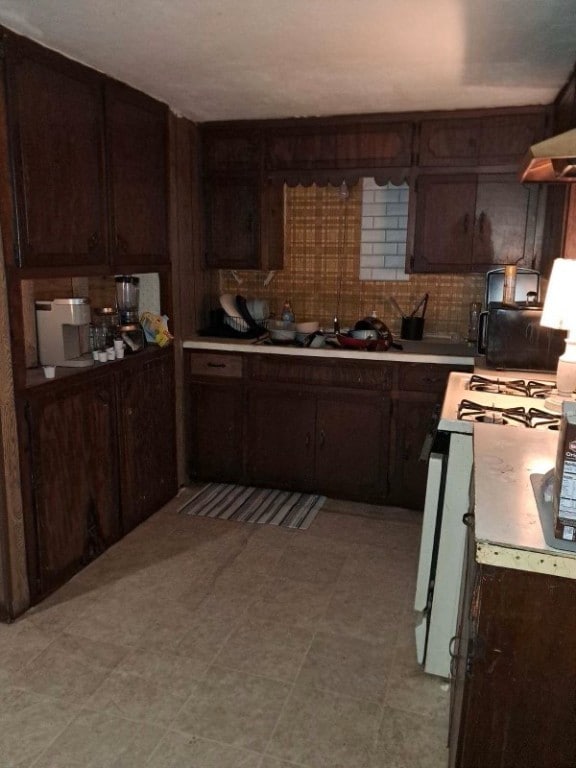 kitchen with sink, backsplash, dark brown cabinetry, and white gas range oven