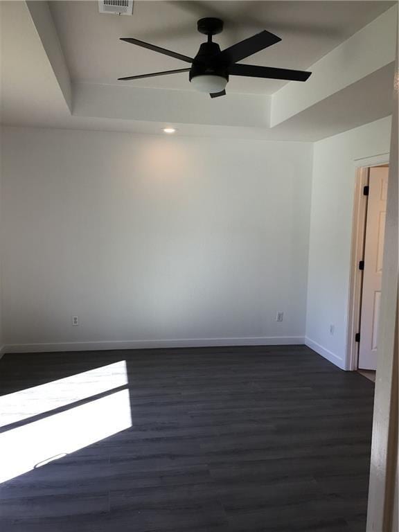 unfurnished room with a tray ceiling, dark hardwood / wood-style floors, and ceiling fan