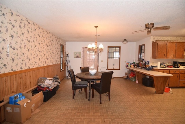 dining room featuring ceiling fan with notable chandelier, wooden walls, and a textured ceiling