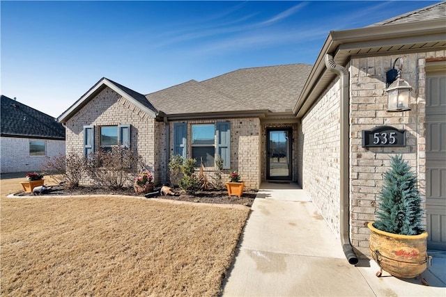 doorway to property with brick siding and roof with shingles