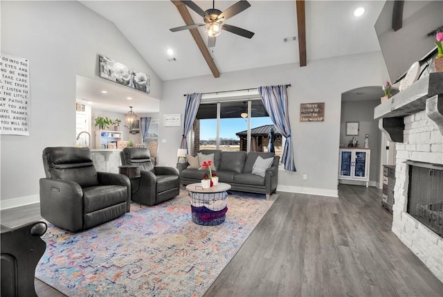 living room featuring hardwood / wood-style flooring, ceiling fan, a stone fireplace, and lofted ceiling with beams