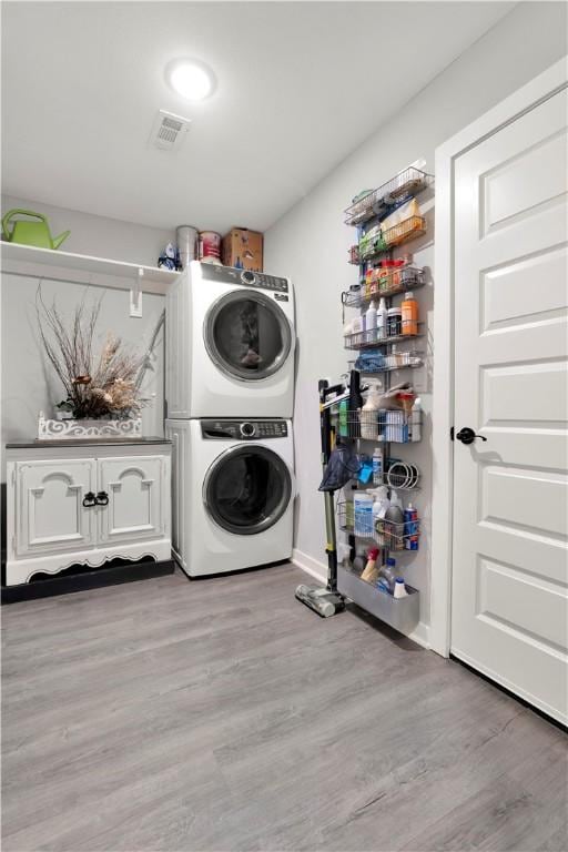 washroom featuring cabinets, stacked washer and dryer, and light hardwood / wood-style flooring