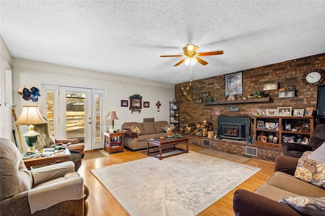 living room featuring ceiling fan, light hardwood / wood-style floors, a textured ceiling, and a wood stove